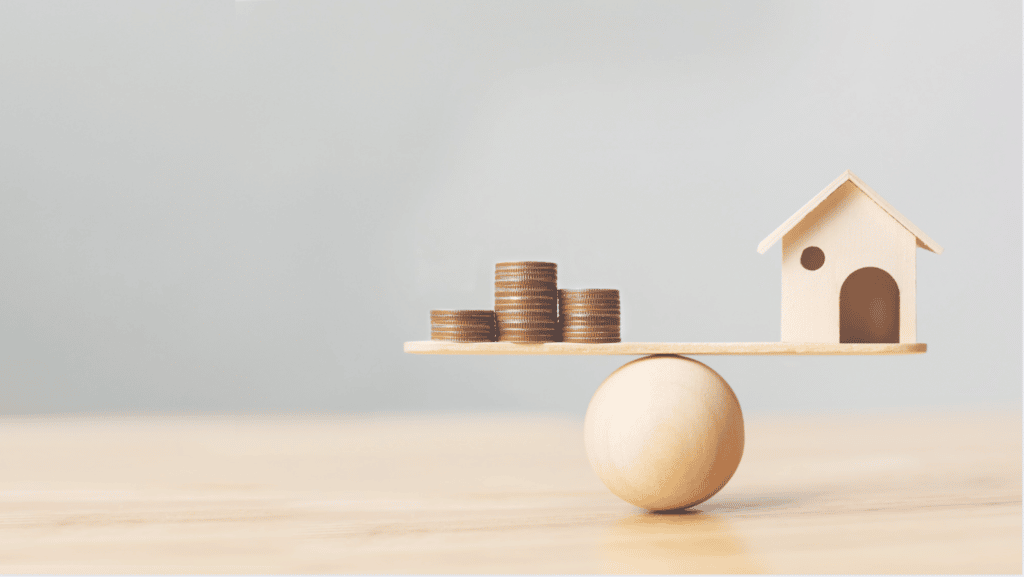 Wooden home and coins balanced on a see-saw, depicting balanced home value.